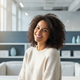 A smiling woman in her late 20s in a modern office setting, representing a happy, diverse customer.